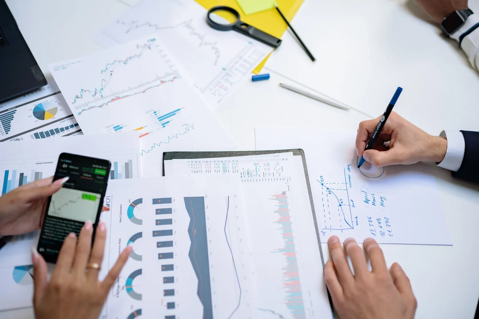 Hands using a smartphone and reviewing charts on an office table