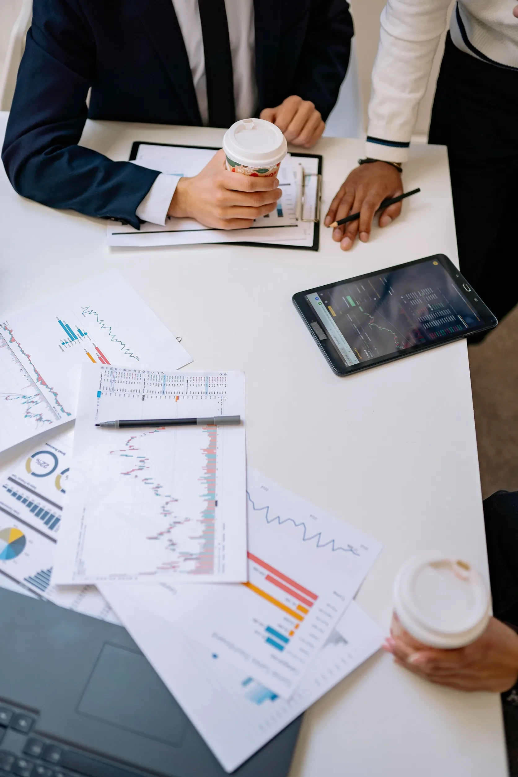 High-angle office table with charts, coffee, and tablet during a planning session
